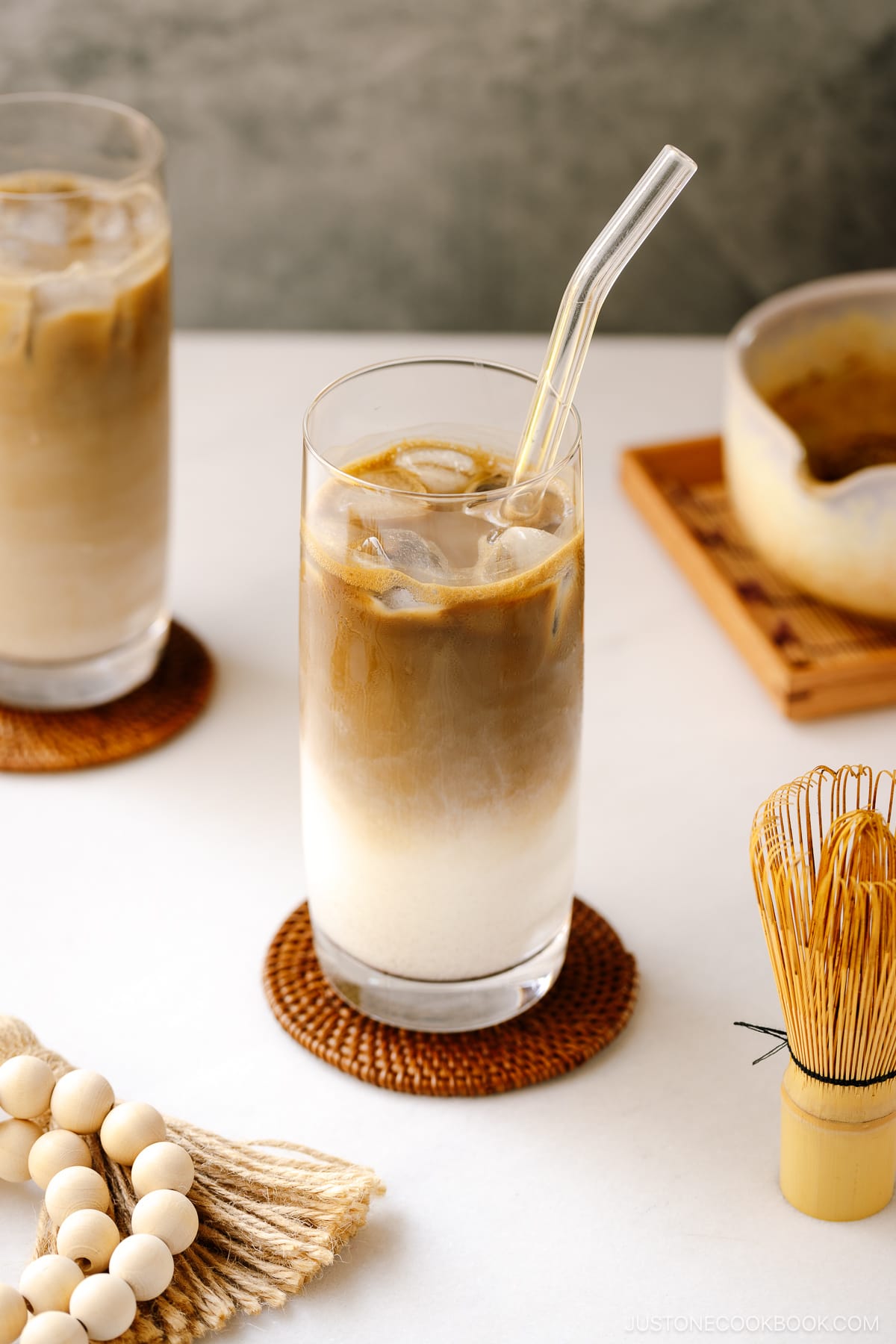 A tall glass filled with iced hojicha latte, showing two layers of milk and chocolate-color roasted green tea (hojicha).