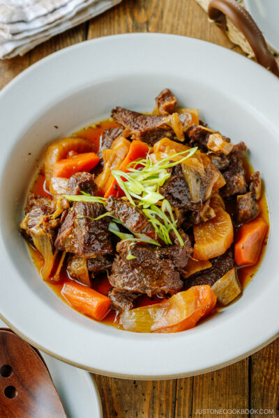 A white ceramic bowl containing Instant Pot Short Ribs with daikon and carrots pressure cooked in a savory sauce.