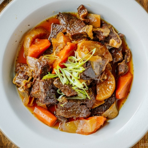 A white ceramic bowl containing Instant Pot Short Ribs with daikon and carrots pressure cooked in a savory sauce.