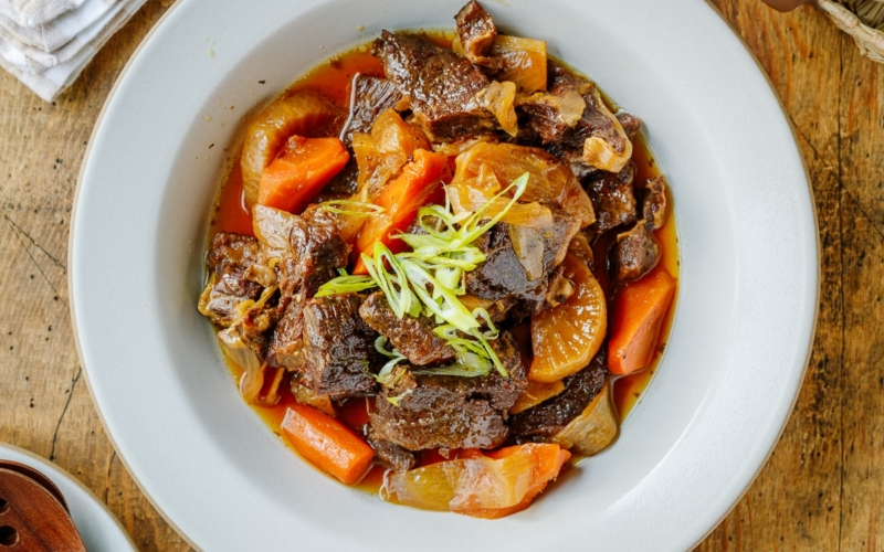 A white ceramic bowl containing Instant Pot Short Ribs with daikon and carrots pressure cooked in a savory sauce.