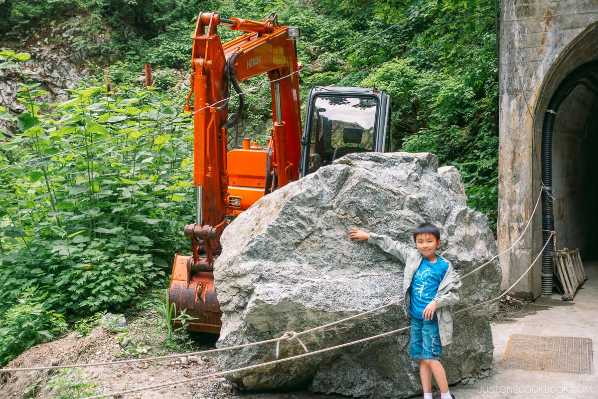a boy standing next to a large stone boulder