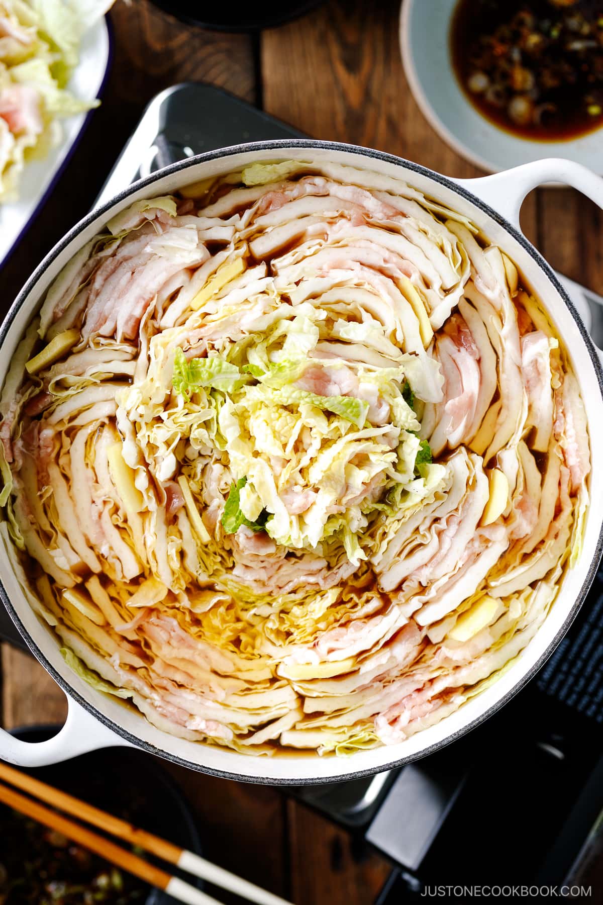 A Le Creuset pot containing Mille-Feuille Nabe, which is a hot pot dish with layers of pork belly slices and napa cabbage slices in a dashi broth.