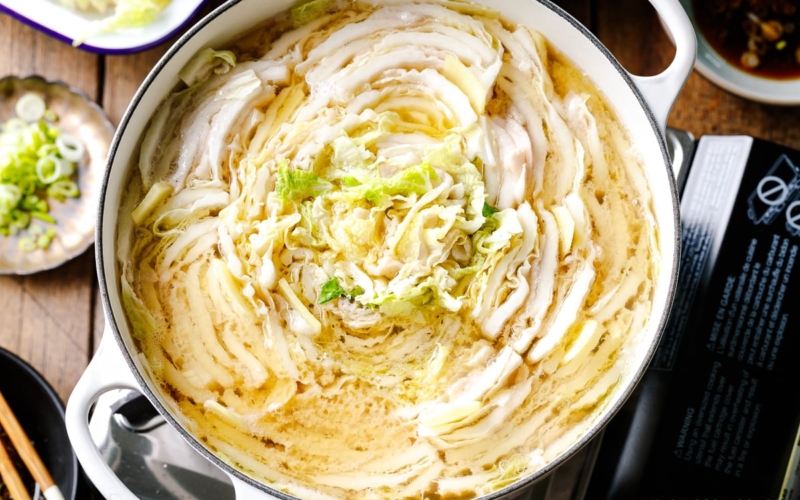 A Le Creuset pot containing Mille-Feuille Nabe, which is a hot pot dish with layers of pork belly slices and napa cabbage slices in a dashi broth.