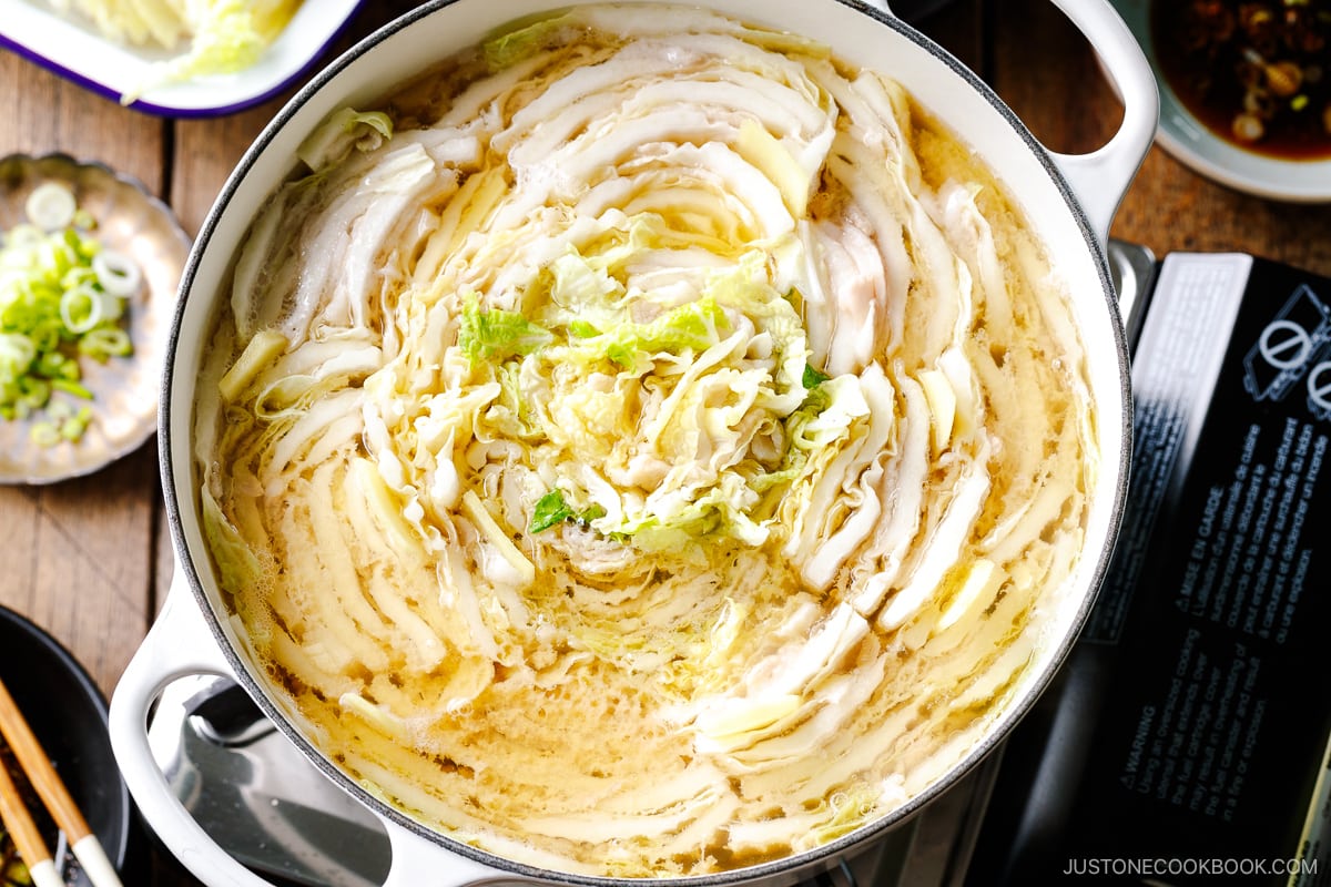 A Le Creuset pot containing Mille-Feuille Nabe, which is a hot pot dish with layers of pork belly slices and napa cabbage slices in a dashi broth.