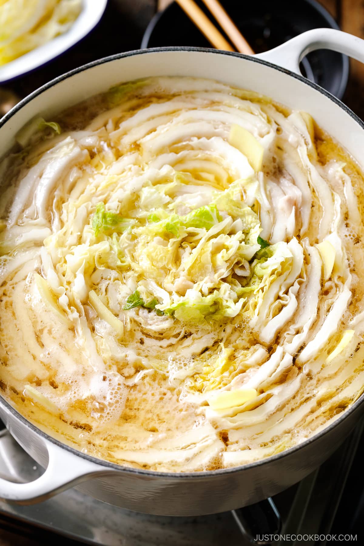 A Le Creuset pot containing Mille-Feuille Nabe, which is a hot pot dish with layers of pork belly slices and napa cabbage slices in a dashi broth.