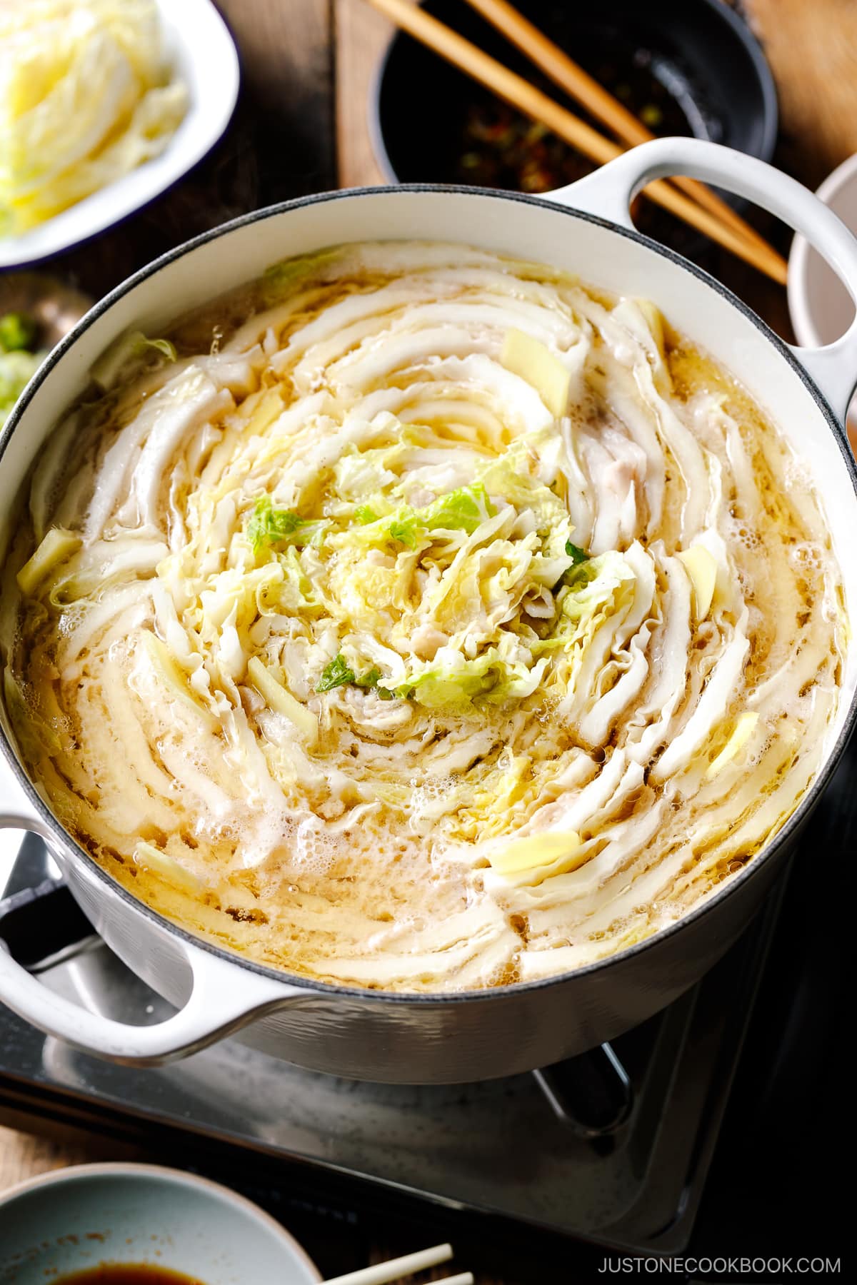 A Le Creuset pot containing Mille-Feuille Nabe, which is a hot pot dish with layers of pork belly slices and napa cabbage slices in a dashi broth.