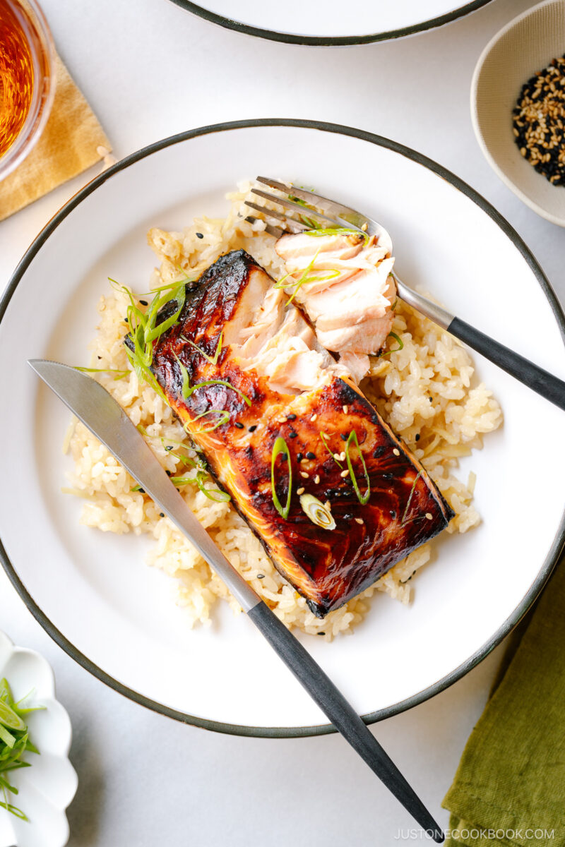 A white plate containing Broiled Miso Salmon served over ginger rice.