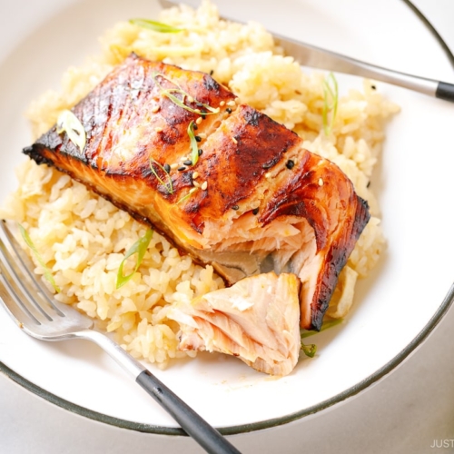 A white plate containing Broiled Miso Salmon served over ginger rice.