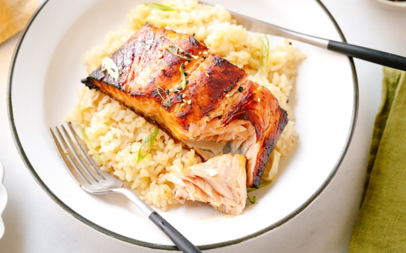 A white plate containing Broiled Miso Salmon served over ginger rice.