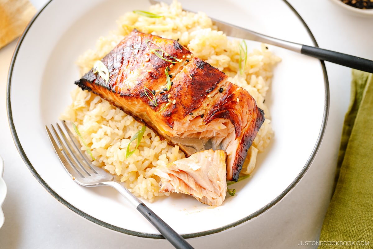 A white plate containing Broiled Miso Salmon served over ginger rice.