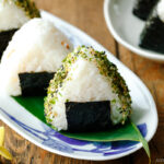 An oval plate containing 3 pieces of Onigiri (Japanese Rice Balls) placed on a bamboo leaf.