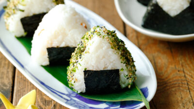 An oval plate containing 3 pieces of Onigiri (Japanese Rice Balls) placed on a bamboo leaf.