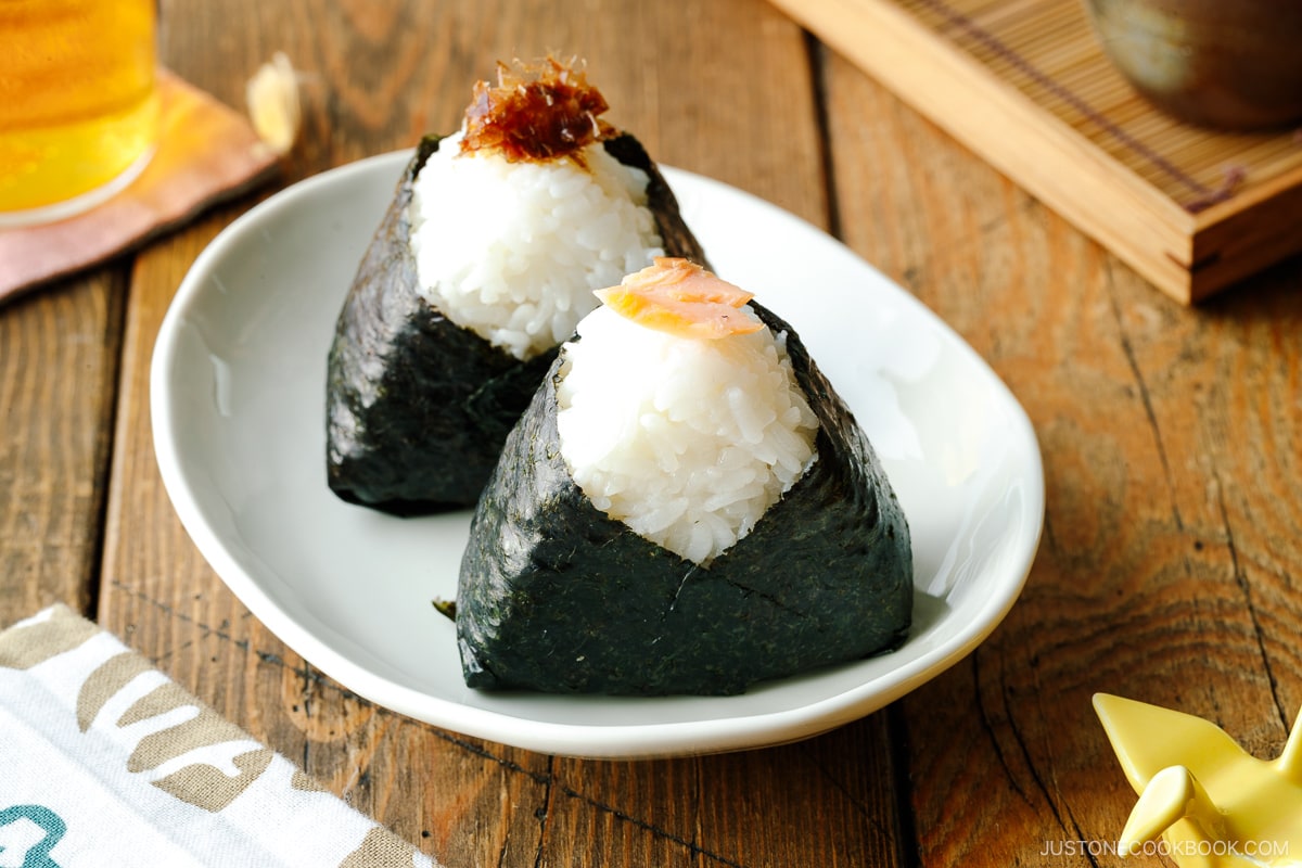 A plate containingn 2 onigiri (Japanese rice balls) garnished with bonito flakes and salmon on top.