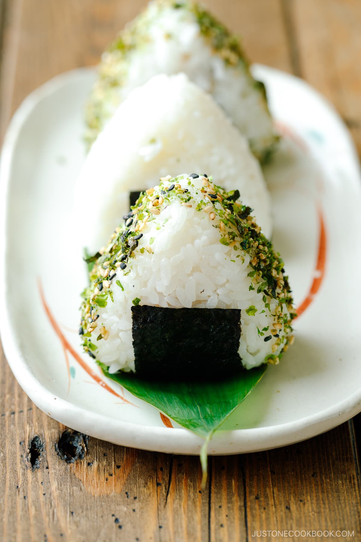 An oval plate containing 3 pieces of Onigiri (Japanese Rice Balls) placed on a bamboo leaf.