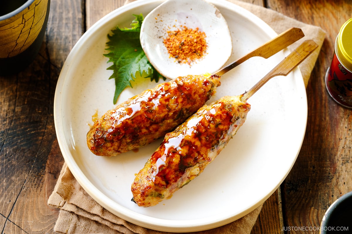 A white plate containing two skewers of Tsukune (Japanese chicken meatball) accompanied by shichimi togarashi, Japanese seven spices.