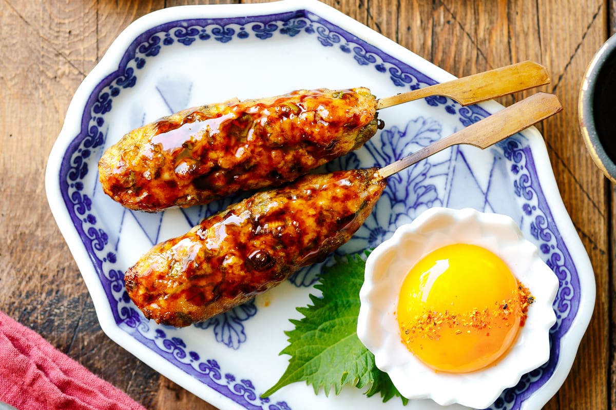 A Japanese ceramic plate containing two skewers of Tsukune (Japanese chicken meatball) accompanied by shichimi togarashi, Japanese seven spices.