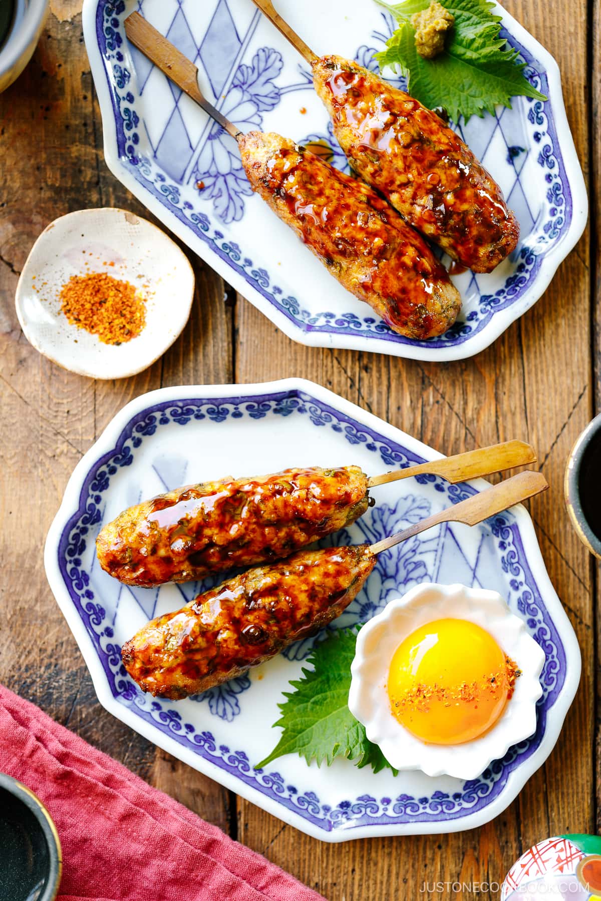 Japanese ceramic plates containing two skewers of Tsukune (Japanese chicken meatball) accompanied by shichimi togarashi, Japanese seven spices.