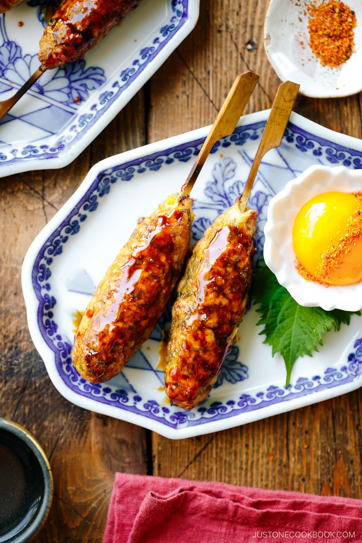 Japanese ceramic plates containing two skewers of Tsukune (Japanese chicken meatball) accompanied by shichimi togarashi, Japanese seven spices.