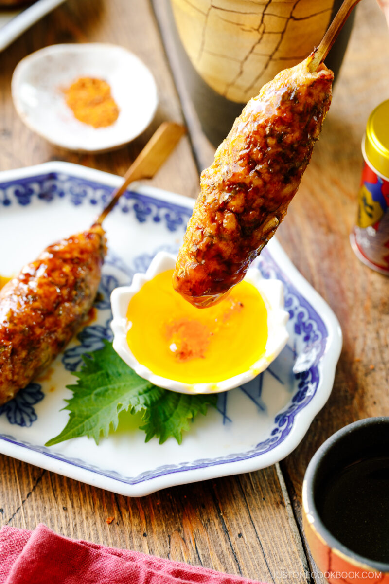 Japanese ceramic plates containing two skewers of Tsukune (Japanese chicken meatball) accompanied by shichimi togarashi, Japanese seven spices.