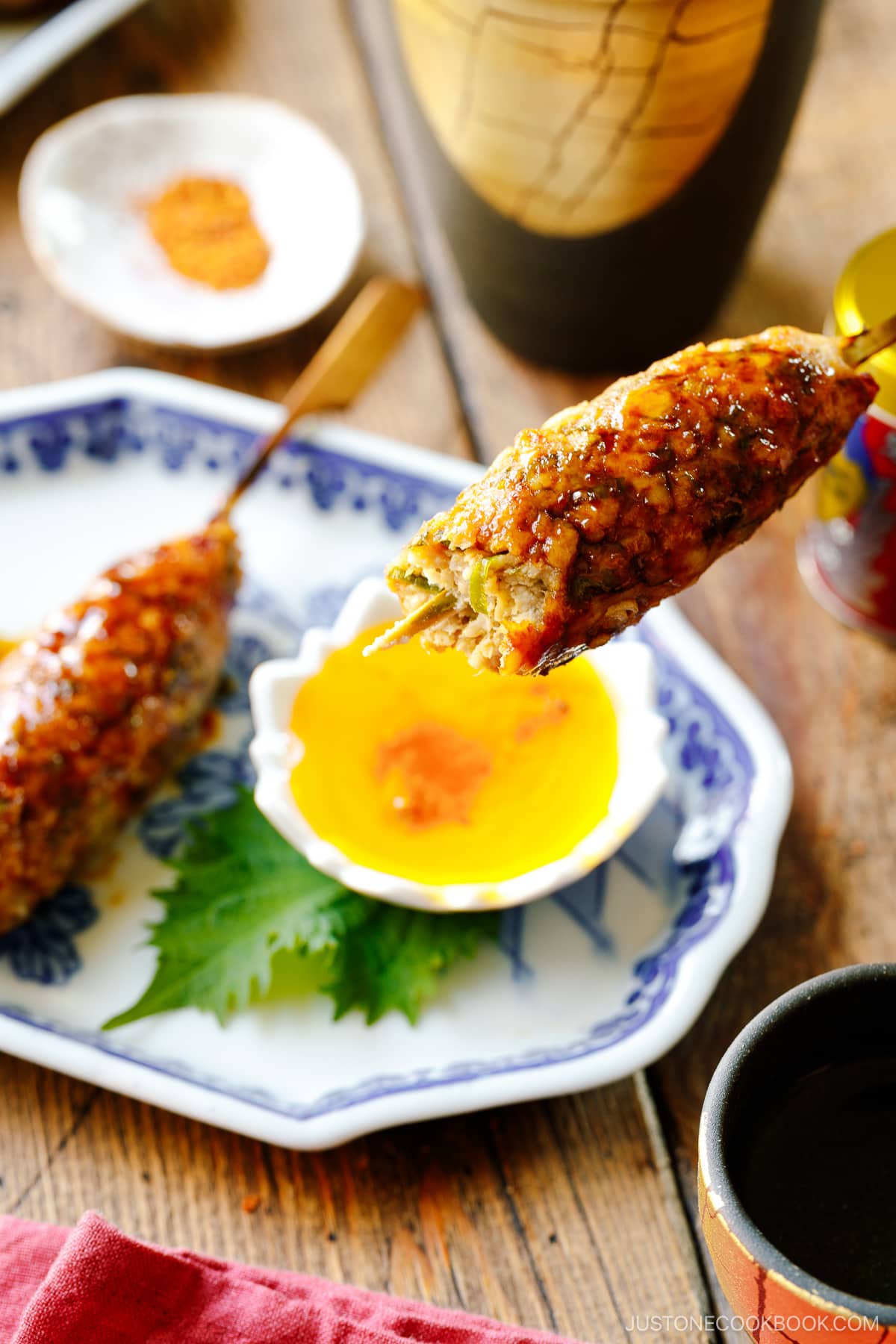 Japanese ceramic plates containing two skewers of Tsukune (Japanese chicken meatball) accompanied by shichimi togarashi, Japanese seven spices.