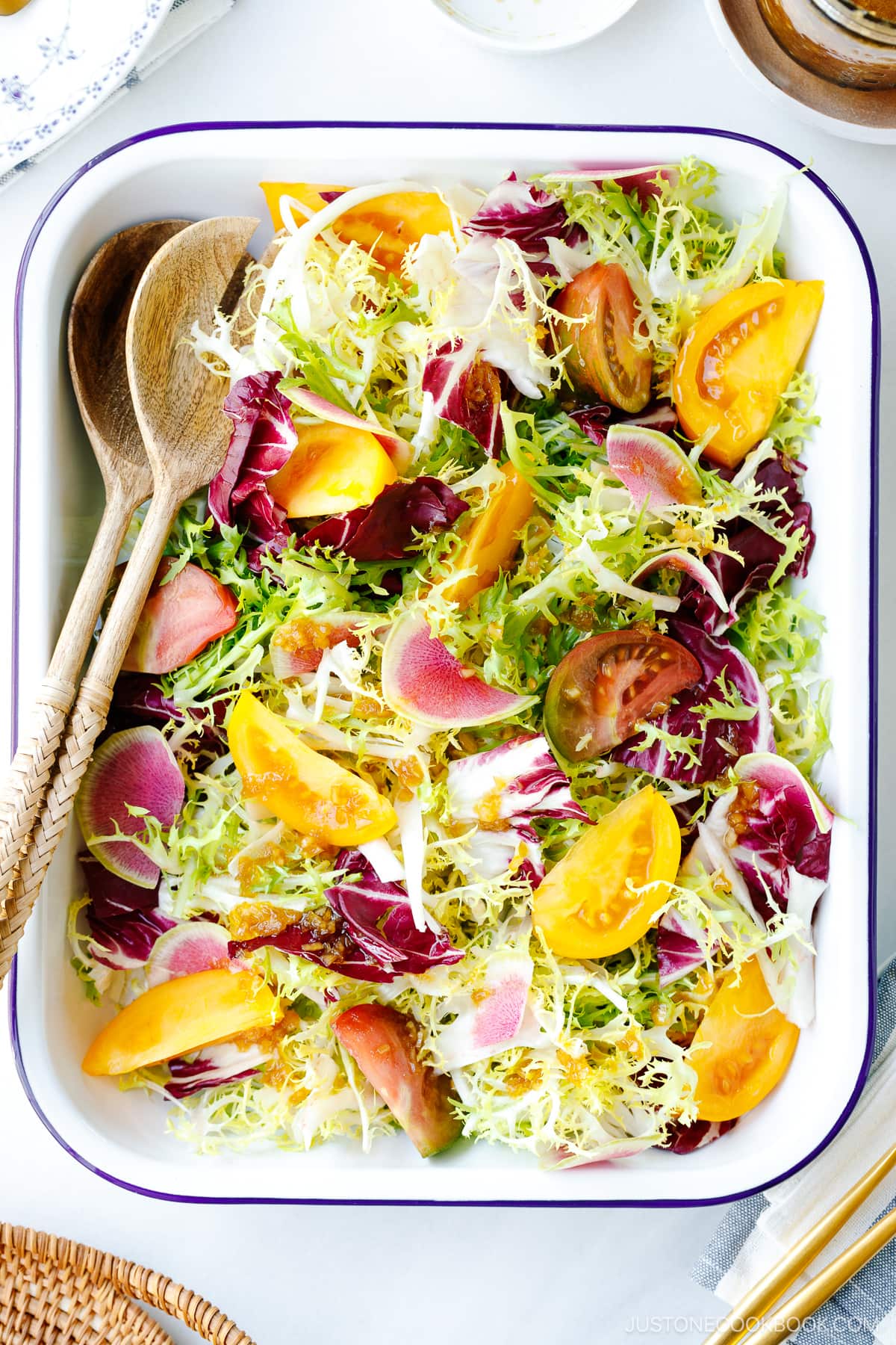 A white and blue enamel tray containing frisee and radicchio lettuce, thinly sliced watermelon radish, and heirloom tomatoes, drizzled with Japanese onion dressing.