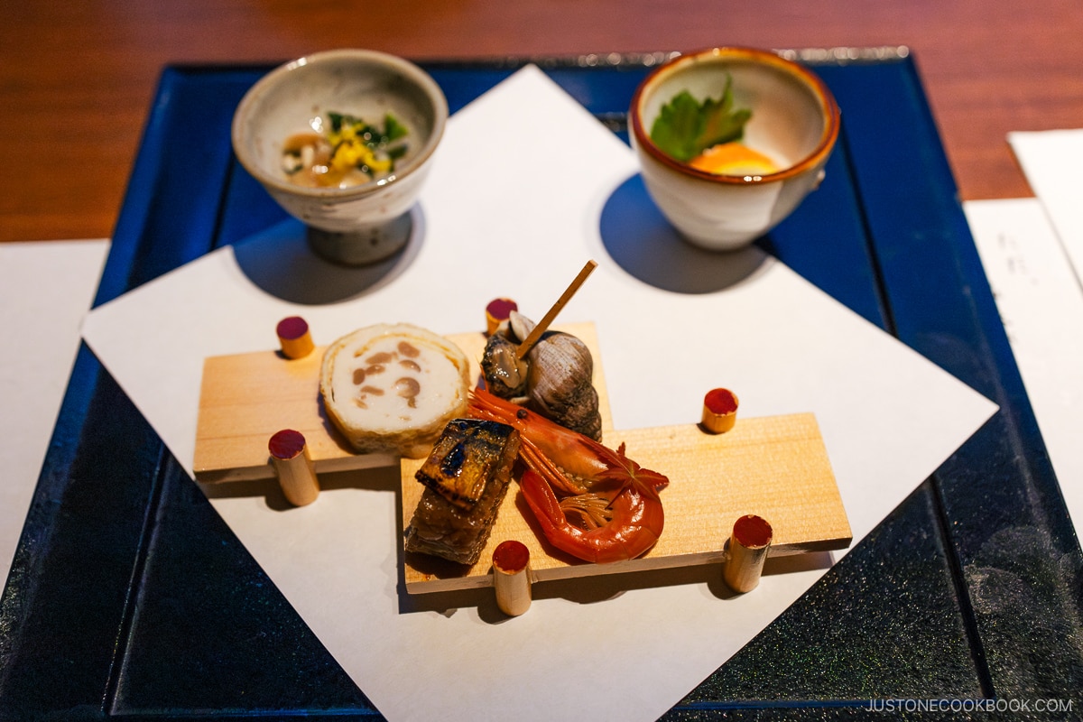 Hotel dinner appetizer of Shima ebi (shrimp), Pacific saury, marinated salmon, fish cake wrapped in deep-fried tofu, whelk, boiled seasoned mushrooms.