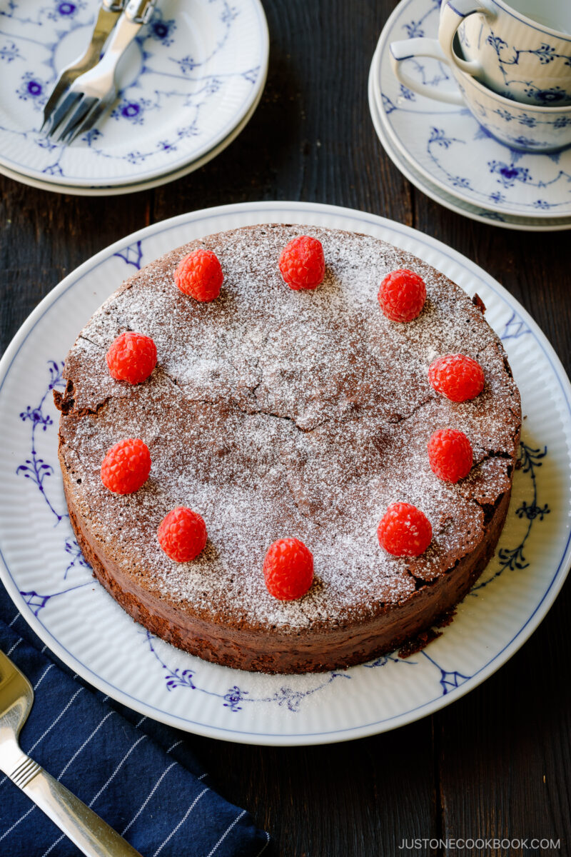 A large plate containing Chocolate Gateau (Chocolate Cake) dusted with powdered sugar and decorated with raspberries.