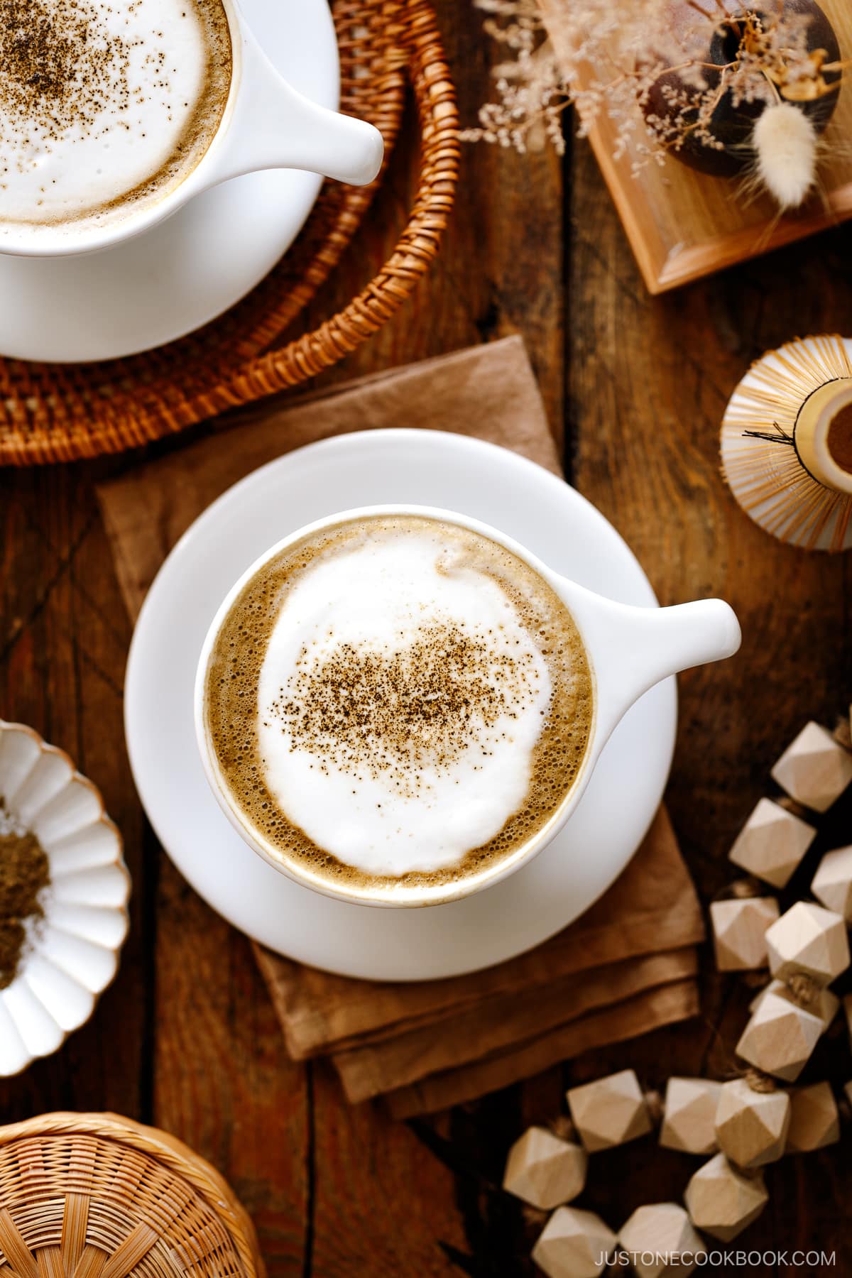 White cups containing Hojicha Latte topped with roasted green tea powder.