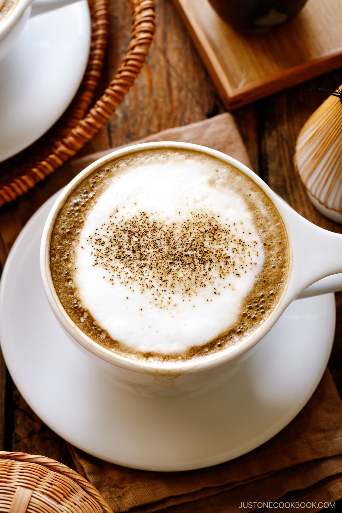 White cups containing Hojicha Latte topped with roasted green tea powder.