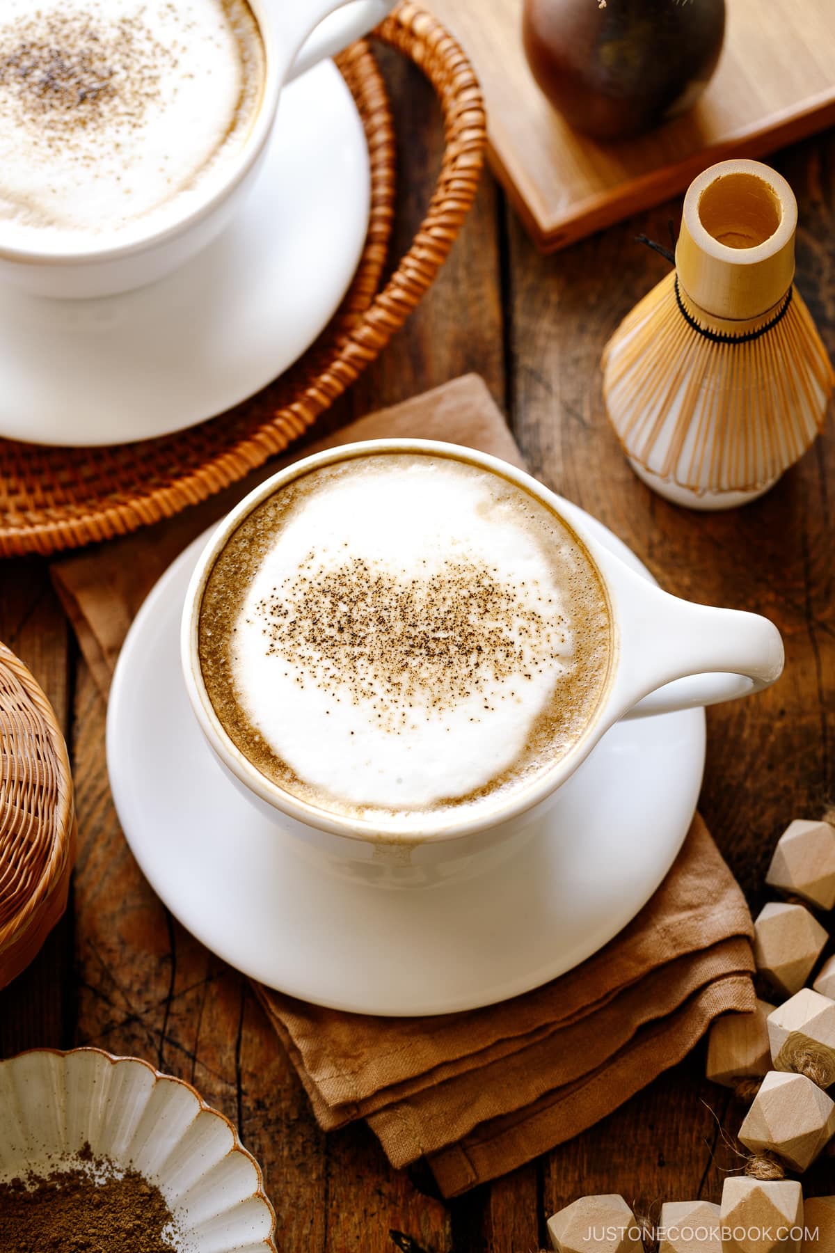 White cups containing Hojicha Latte topped with roasted green tea powder.