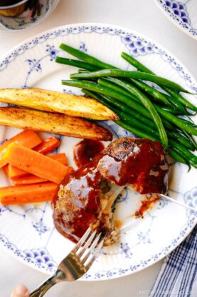 A white and blue plate containing Cheese Stuffed Japanese Hamburger Steak (Hambagu) stuffed with cheese and slathered in demi-glace sauce.