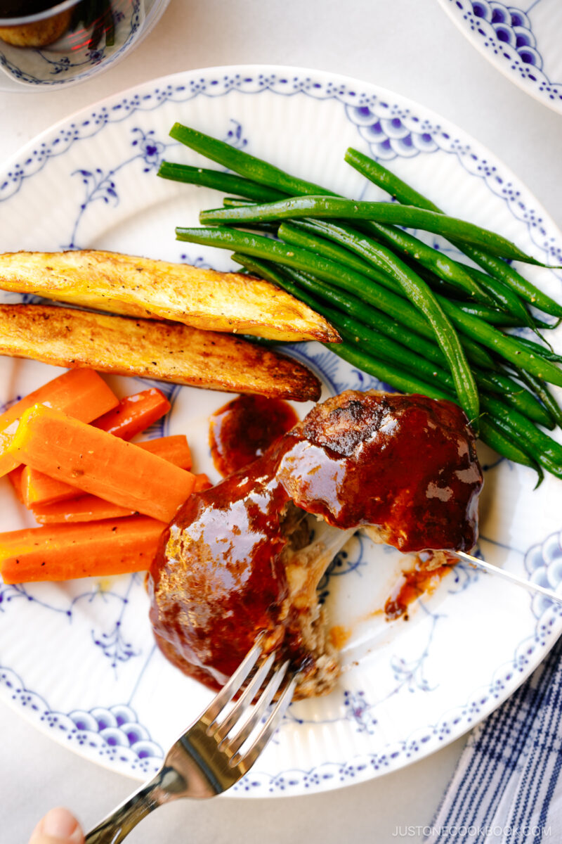 A white and blue plate containing Cheese Stuffed Japanese Hamburger Steak (Hambagu) stuffed with cheese and slathered in demi-glace sauce.