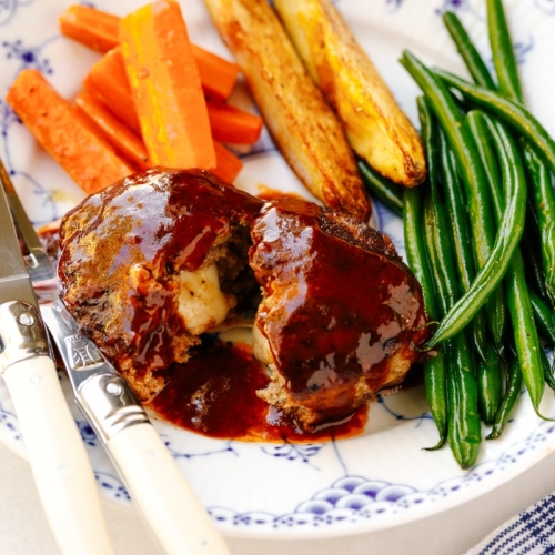 A white and blue plate containing Cheese Stuffed Japanese Hamburger Steak (Hambagu) stuffed with cheese and slathered in demi-glace sauce.