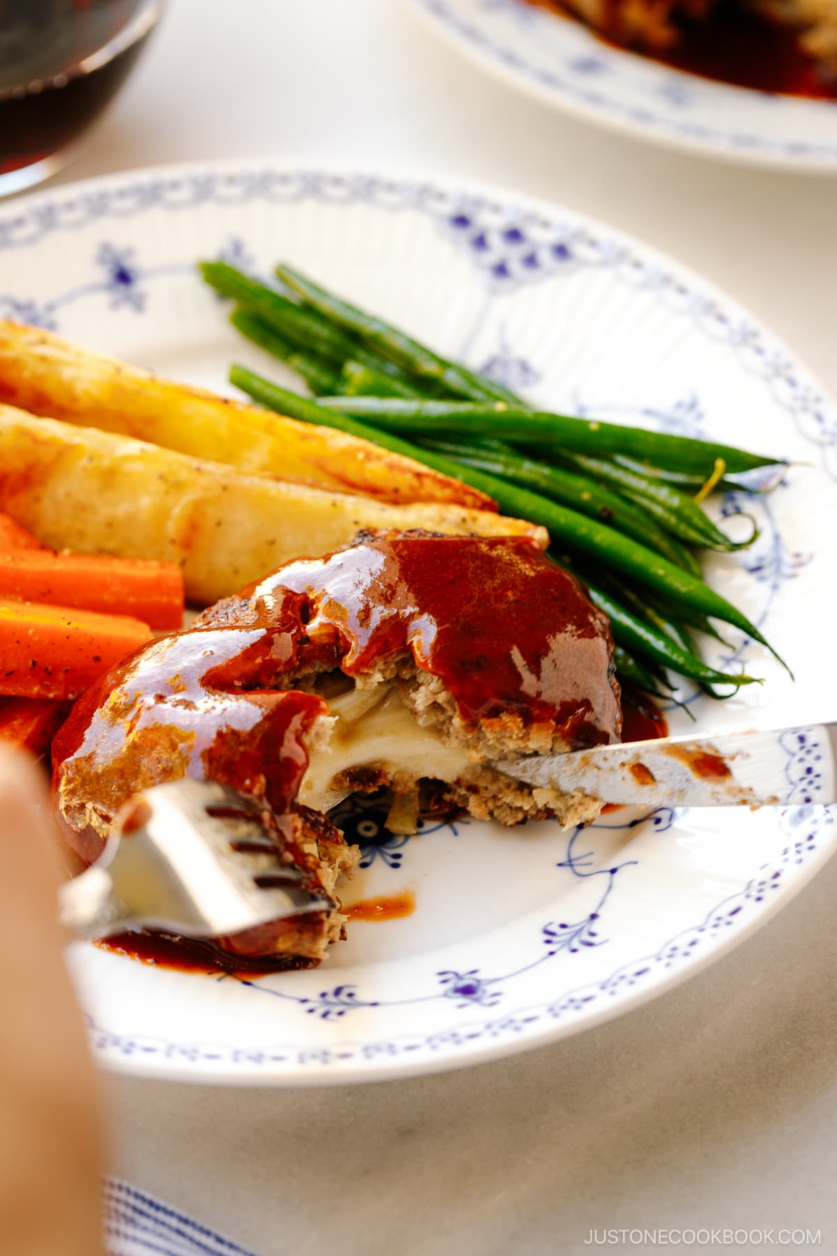 A white and blue plate containing Cheese Stuffed Japanese Hamburger Steak (Hambagu) stuffed with cheese and slathered in demi-glace sauce.