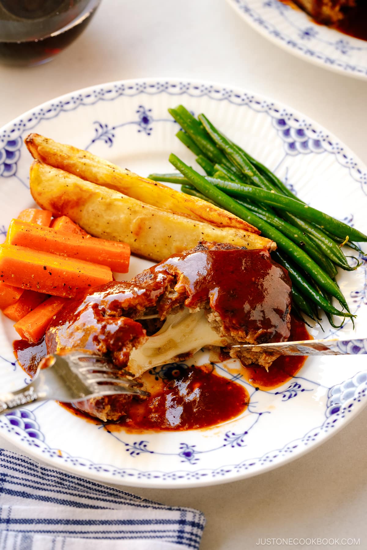 A white and blue plate containing Cheese Stuffed Japanese Hamburger Steak (Hambagu) stuffed with cheese and slathered in demi-glace sauce.