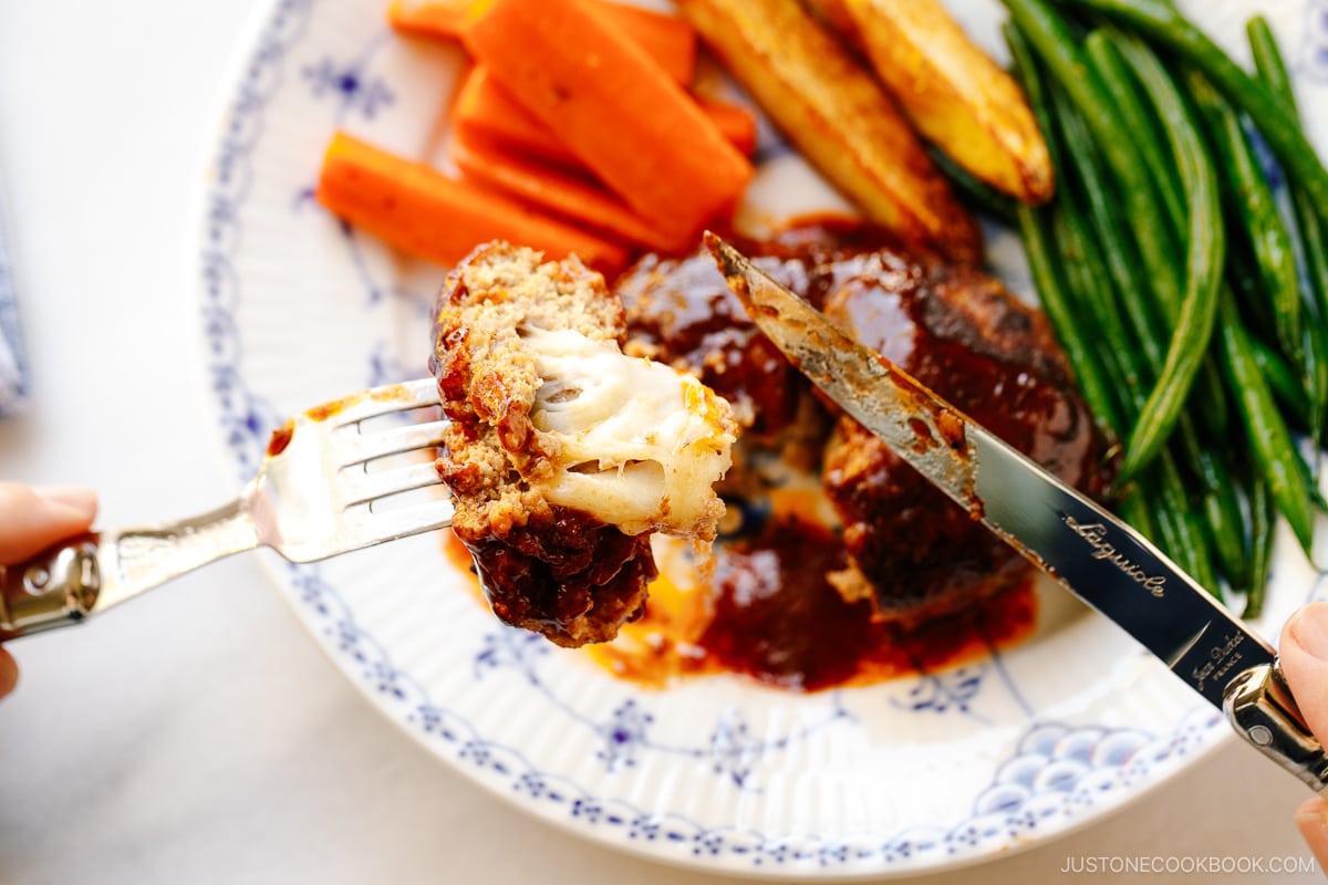 A white and blue plate containing Cheese Stuffed Japanese Hamburger Steak (Hambagu) stuffed with cheese and slathered in demi-glace sauce.