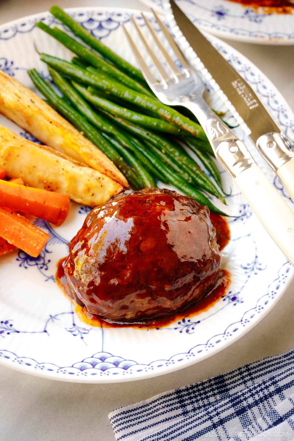 A white and blue plate containing Cheese Stuffed Japanese Hamburger Steak (Hambagu) stuffed with cheese and slathered in demi-glace sauce.