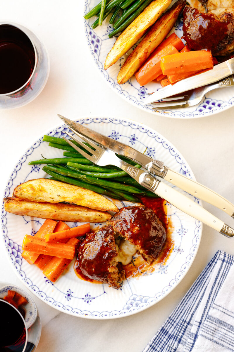 A white and blue plate containing Cheese Stuffed Japanese Hamburger Steak (Hambagu) stuffed with cheese and slathered in demi-glace sauce.