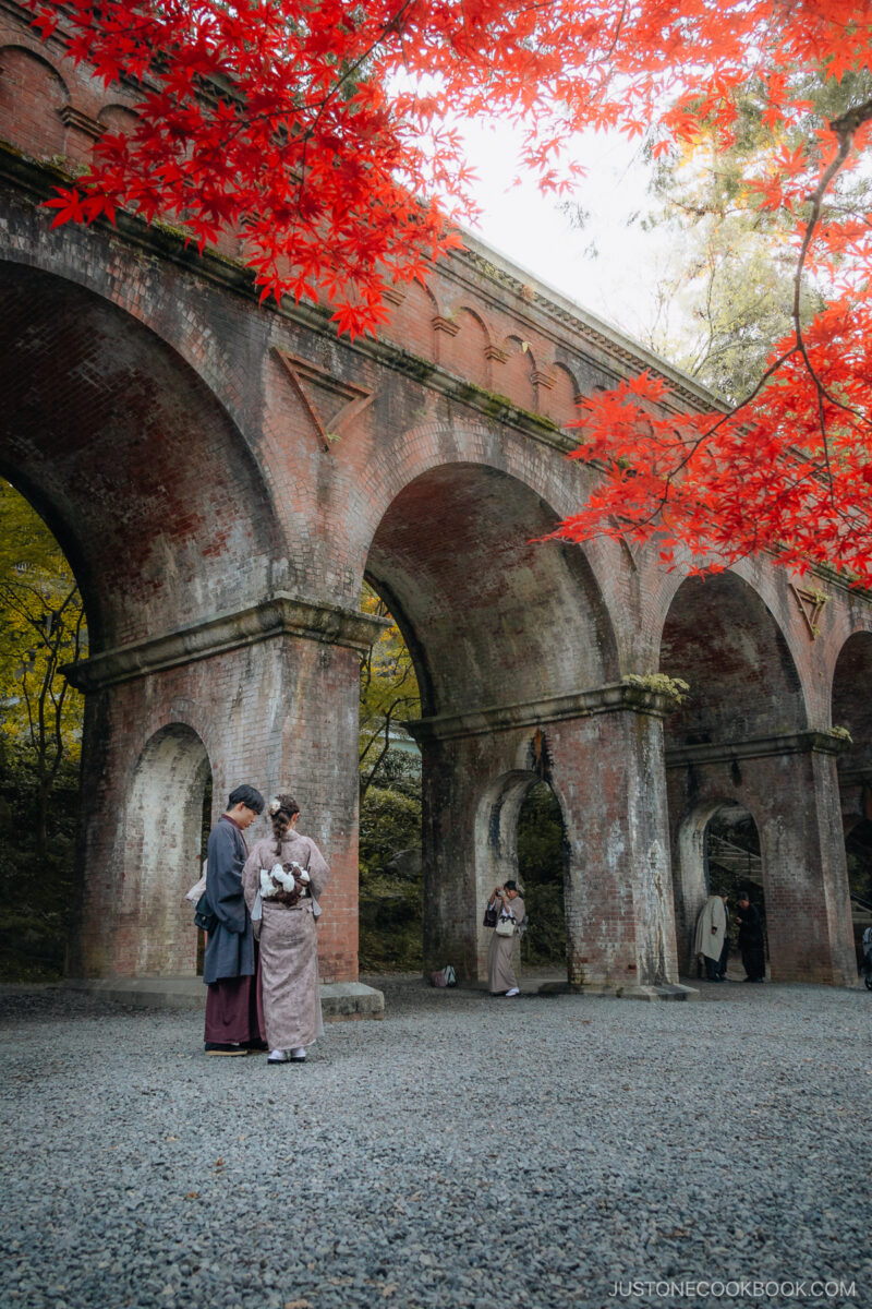 Red brick bridge with red autumn leaves and two people in kimonos