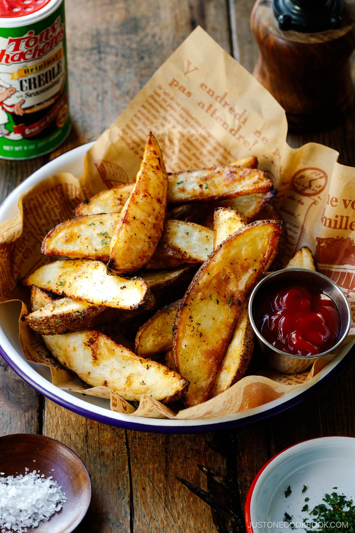 A white and blue enamel bowl containing Crispy Baked Potato Wedges with ketchu in a mini container.