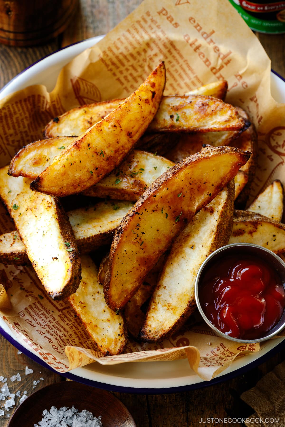 A white and blue enamel bowl containing Crispy Baked Potato Wedges with ketchu in a mini container.