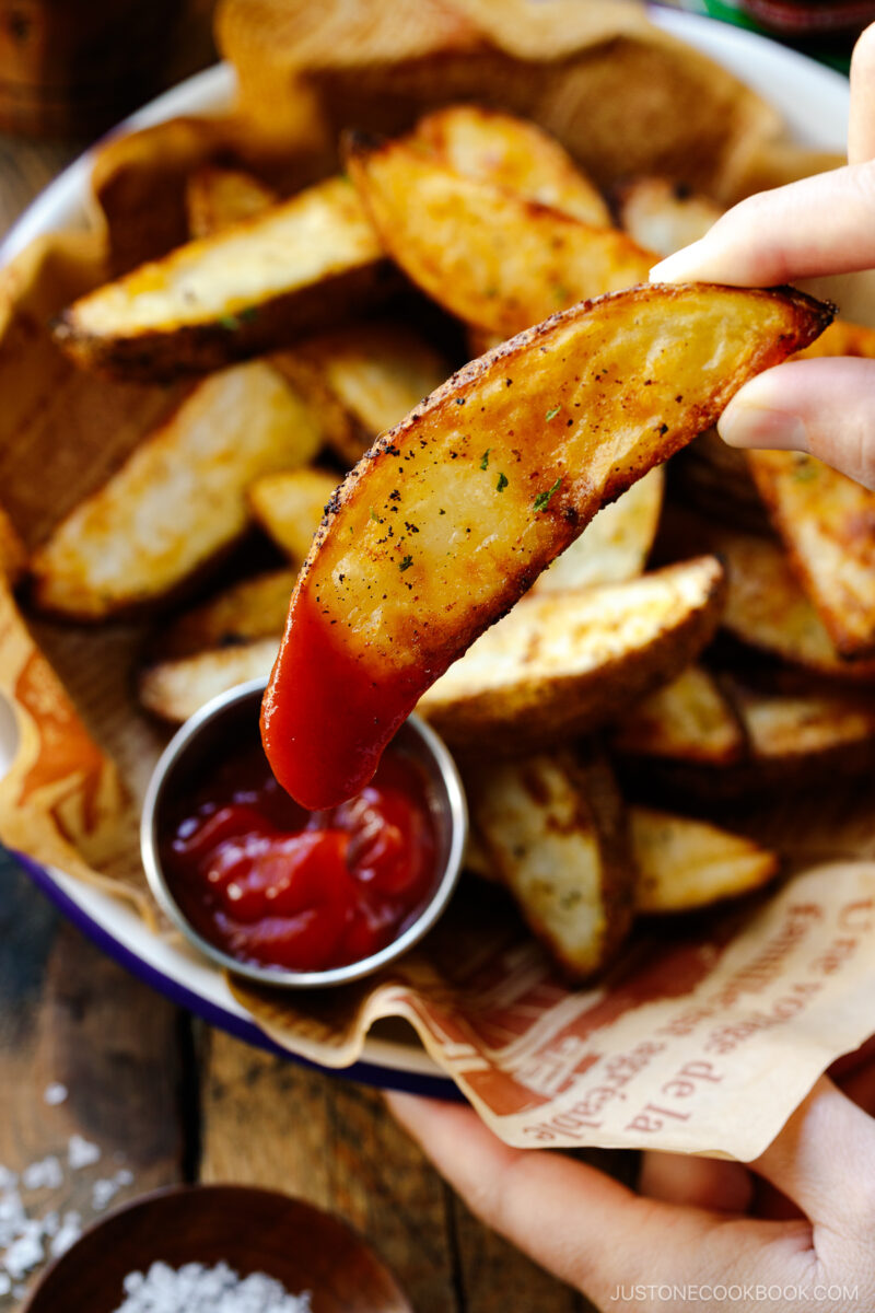 A white and blue enamel bowl containing Crispy Baked Potato Wedges with ketchu in a mini container.