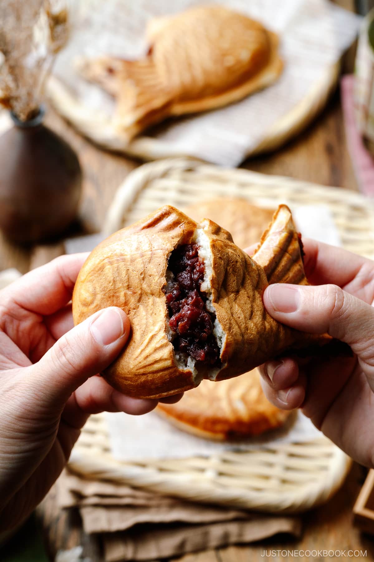 Hands breaking Taiyaki, fish-shaped cake, in half, exposing the sweet red bean filling.