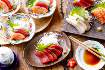 Multiple plates containing sashimi grade fish, including salmon, tuna, and kanpachi, garnished with shredded daikon, shiso leaves, and wasabi.