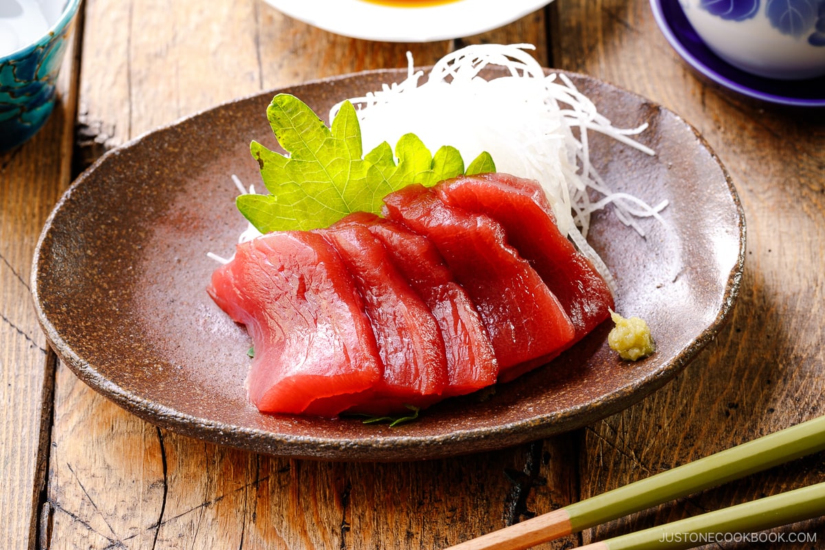A plate containing sashimi grade tuna, garnished with shredded daikon, shiso leaves, and wasabi.