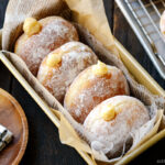 A baking pan containing Nama Donuts, dusted with powdered sugar and filled with the custard.