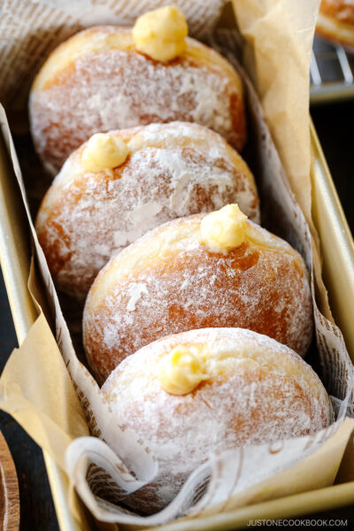 A baking pan containing Nama Donuts, dusted with powdered sugar and filled with the custard.