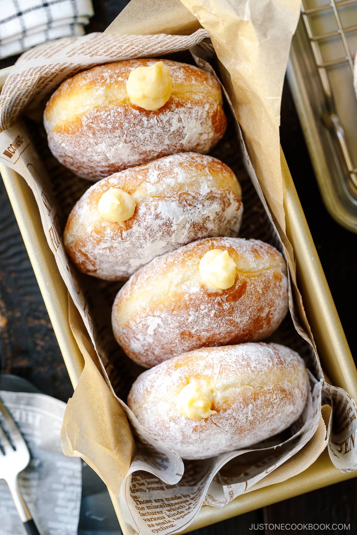 A baking pan containing Nama Donuts, dusted with powdered sugar and filled with the custard.