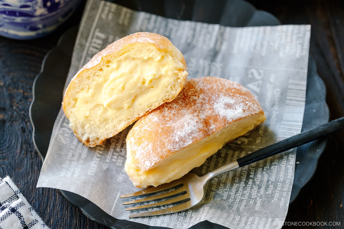 A black fluted plate containing Nama Donuts dusted with powdered sugar and filled with the custard.