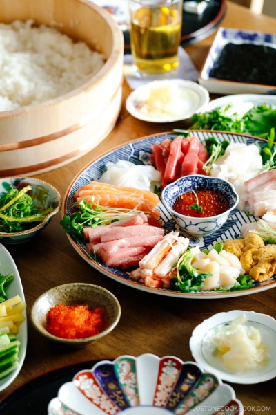 A temaki hand roll sushi spread on the dining table, consisting of plates and bowls containing sushi rice, sashimi, vegetable fillings, and nori seaweed.